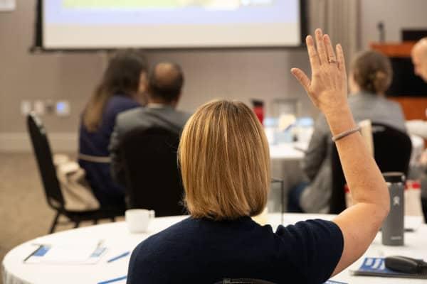 Person raising hand during a small group meeting or workshop in a conference room.